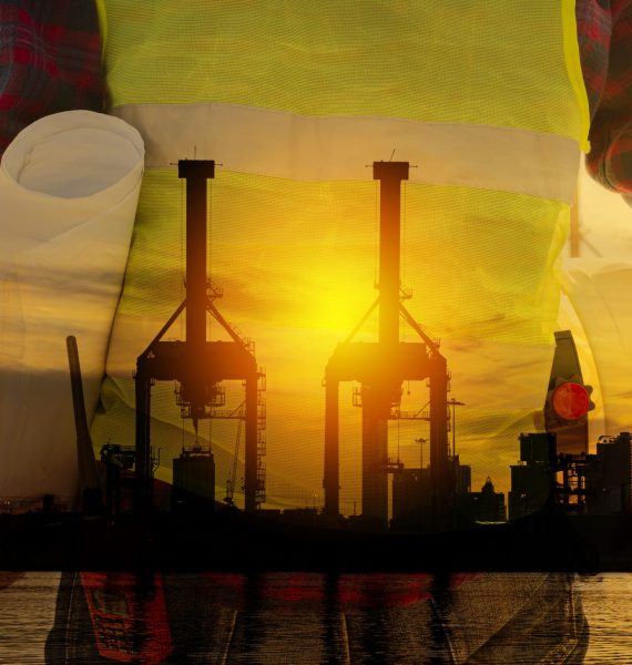 Silhouette of engineers and workers checking the project on the background of the building site, the cargo port at sunset in the evening, the world map